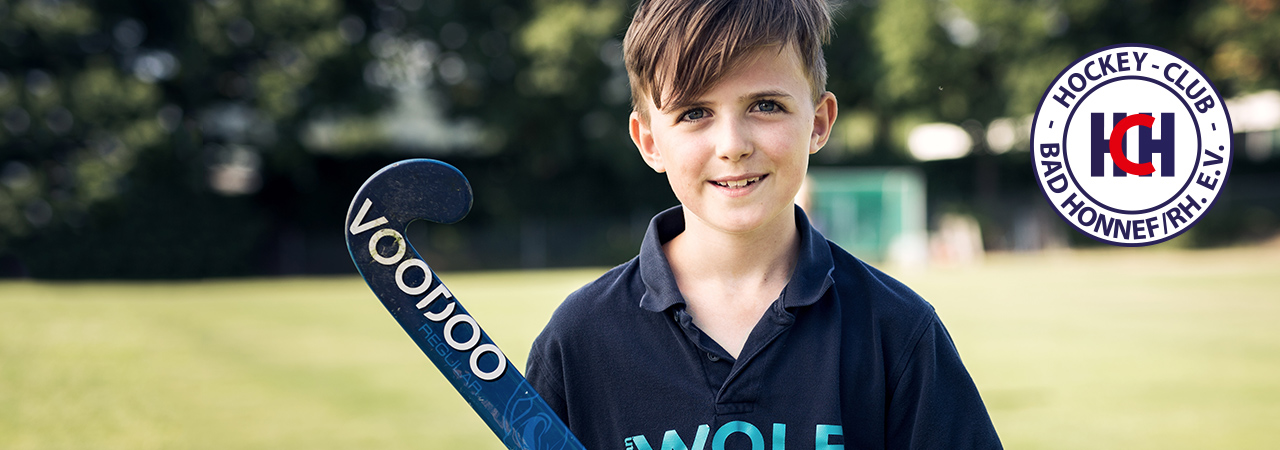Junger Hockey-Spieler im Sonnenuntergang auf blauem Kunstrasen